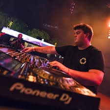 DJ operando una mesa de mezclas Pioneer en un festival nocturno con luces brillantes.